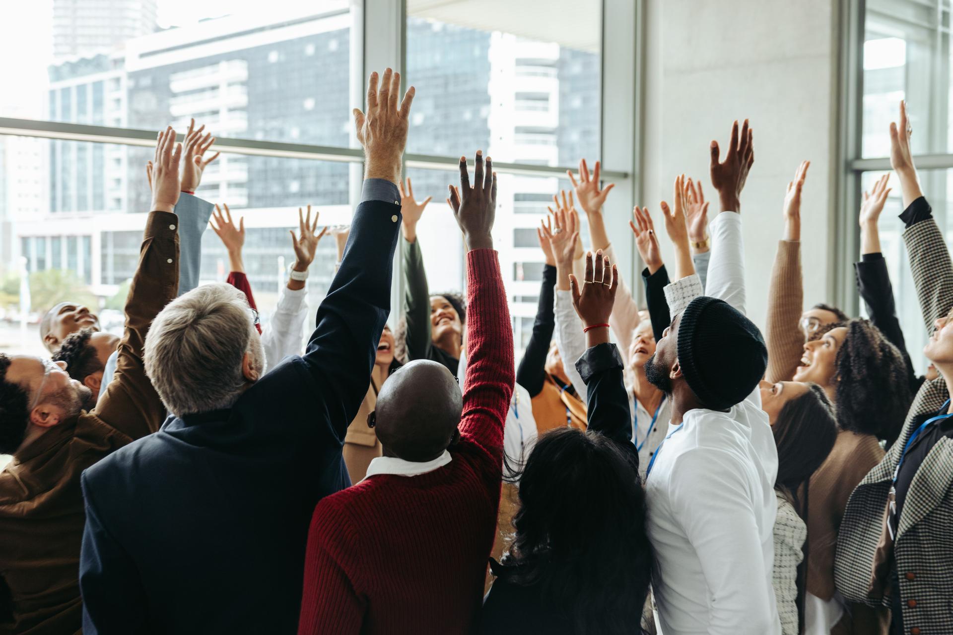 Unity in corporate success as diverse team celebrates achieving goals with hands raised in a modern office setting.