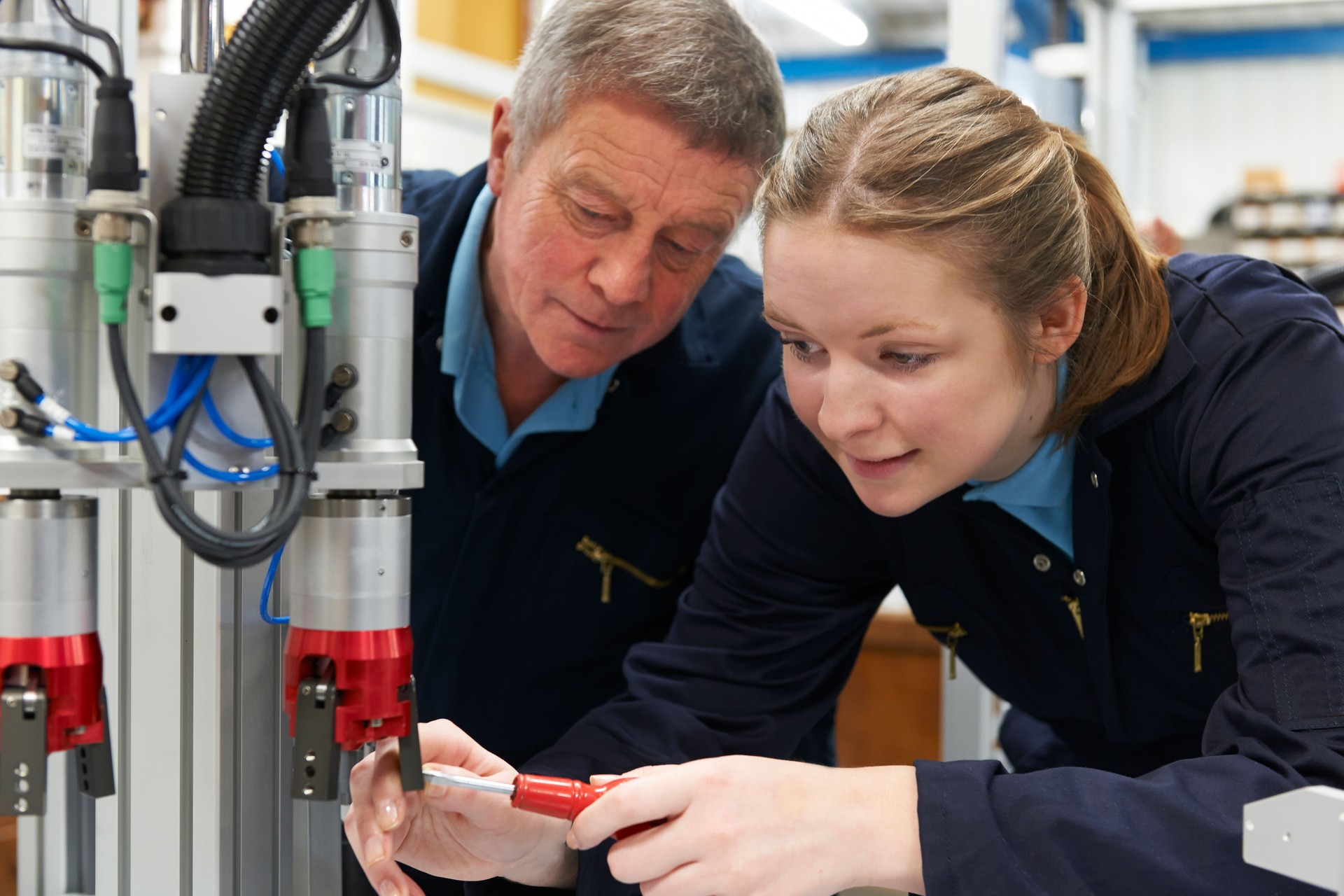 Engineer And Apprentice Working On Machine In Factory