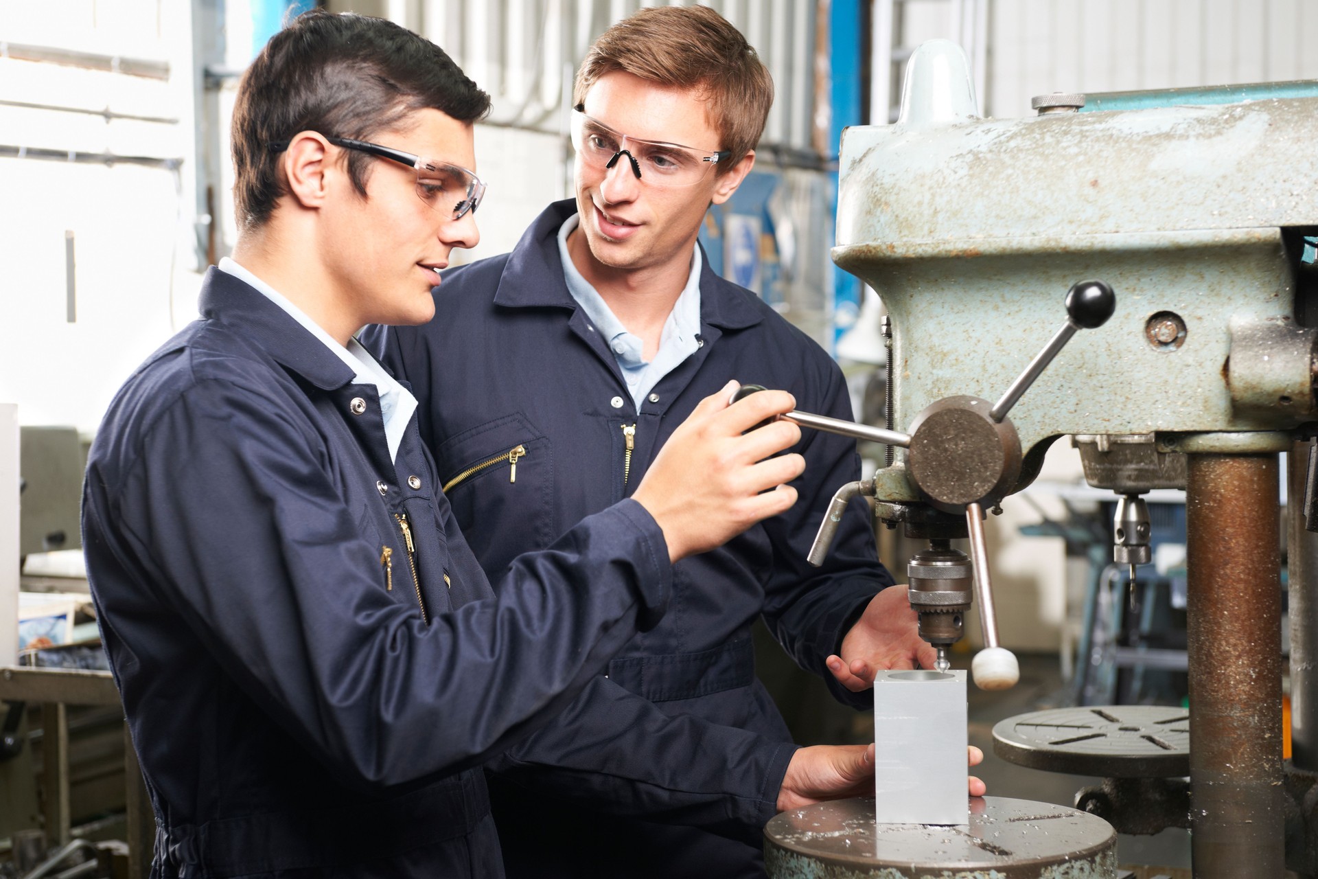 Engineer And Apprentice Using Machinery In Factory